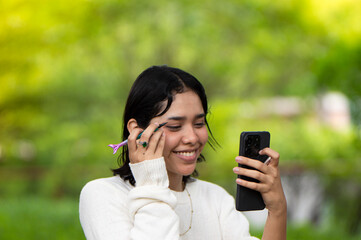 Smiling girl putting on makeup looking her phone
