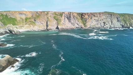 Breathtaking aerial footage of rugged cliffs dramatically rising by the ocean with waves crashing against them