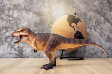 T-rex Dinosaur toy. Tyrannosaurus rex with mini globe on wooden table and dark background bare...