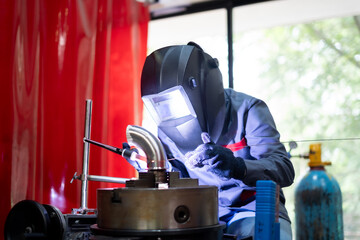 welder working with TIG welding machine on metal pipe in a workshop. Industrial setting with safety gear and precision engineering