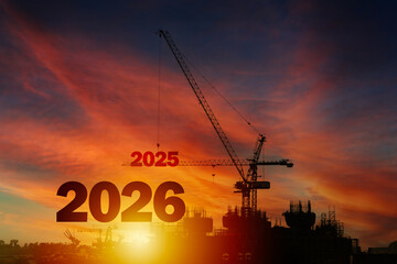 Construction crane lifting 2025 number beside 2026 text at sunset, concept of future building and new beginnings
