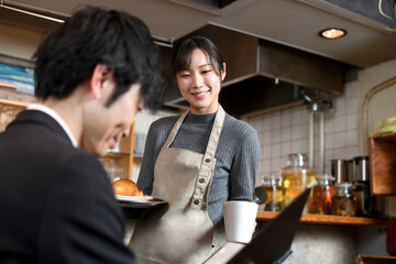 飲食店で男性客に食事の配膳をするアジア人の女性店員