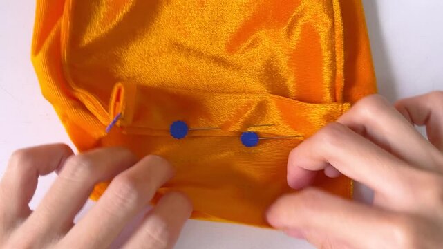 Close-up shot asian woman's hands pinning flower flat head pins on yellow velvet on white table background. Step to make drawstring bag for make merit. Homemade. Bangkok, Thailand./ Slow down video