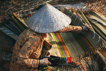 Vietnamese woman worker in traditional straw hat Non La works at a reed weaving mat factory in...