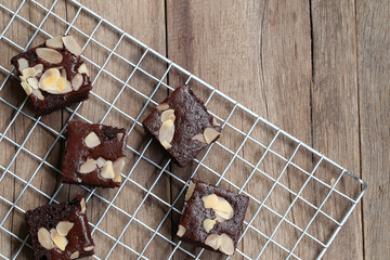 Freshly Baked Chocolate Brownies with Almond Slices on Wire Rack Surrounded by Rustic Wooden Table...