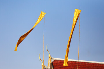 Golden Flags Billowing Against a Blue Sky Above a Traditional Building, Showcasing Cultural...