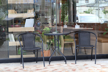 Cozy outdoor seating arrangement featuring two black chairs and a round table beside a glass storefront with plants giving a relaxed ambiance in an urban setting