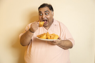 Hungary overweight fat indian man eating unhealthy samosa junk food. Chubby guy starving for fried...