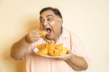Hunger-Excited hungary overweight fat indian man eating unhealthy samosa junk food. Plus size guy...