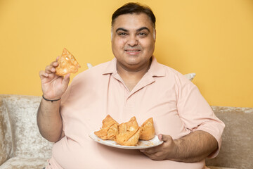 Happy overweight indian man holding plate of samosa snack looking at camera. Plus size guy enjoy fried junk food.