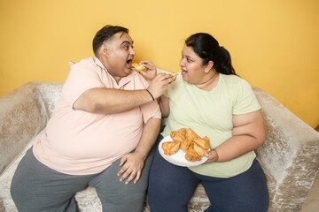 Hungary overweight fat indian couple eating unhealthy samosa junk food together. Plus size husband wife enjoy fried snack. Obese friend sharing high calorie meal. Obesity and weight gain.