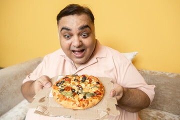 Hungary overweight fat indian man eating cheese pizza. Plus size guy enjoy fatty junk food. Surprised Obese male craving for high calorie meal. Obesity and weight gain.