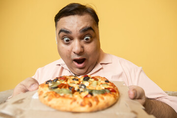 Hungary overweight fat indian man eating cheese pizza. Plus size guy enjoy fatty junk food. Surprised Obese male craving for high calorie meal. Obesity and weight gain.