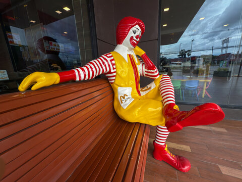 Hua Hin, Thailand - June 15, 2025: Close up wide shot of Ronald McDonald relaxing on bench at McDonald's store exterior