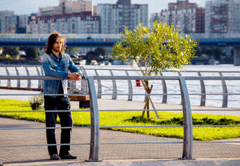 Stylish handsome male model with long hair posing near river on a summer day. Fashion and lifestyle...