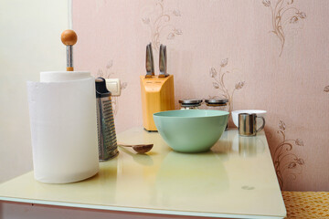 A collection of kitchen utensils are arranged on a table against a floral wall, ready for cooking.