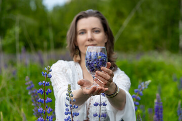 a woman in a white lace dress holding a glass with petals in her hands. She stands against the...