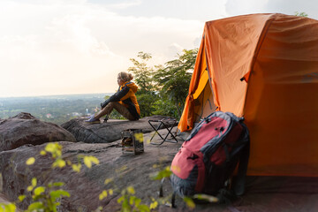 Fototapeta premium A woman sits on a rock next to a tent. She is wearing a yellow jacket