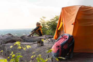 A woman sits on a rock next to a tent. She is wearing a yellow jacket