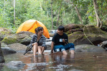A man and a woman sitting in a river. The man is holding a cup