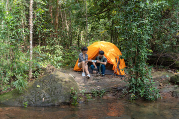 Two people sitting in a tent in the woods. One of them is holding a cup. The tent is orange