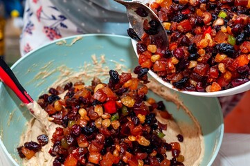 A chef meticulously adding mixed candied fruits into a cake batter bowl, preparing to bake.