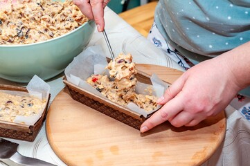 Hands carefully transferring fruitcake batter into loaf pans, ready for baking and enjoying.