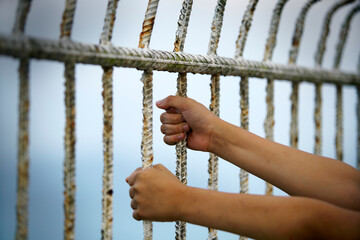 Hands Gripping Iron Bars and Metal Fence Against Soft Sky Background