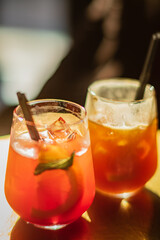 Two vibrant cocktails with fresh ingredients sit elegantly on a wooden table, inviting indulgence