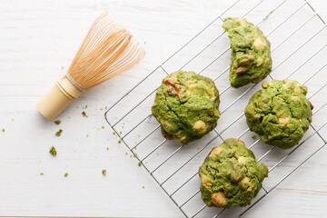 Closeup of fresh baked matcha cookies with Chasen, bamboo whisk, on white wooden background.