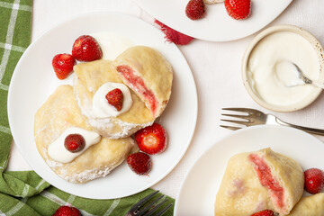Ukrainian vareniki with fresh strawberry filling and sour cream, styled on a white plate. Ideal for...