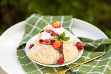 Ukrainian-style varenyky bursting with strawberries. The sliced ones show vibrant red filling — a summer favorite served al fresco.