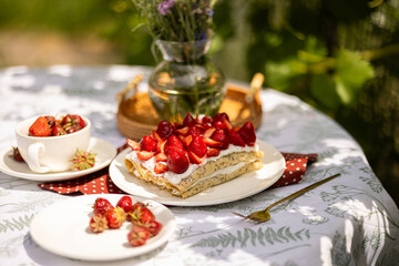Homemade crepe cake with whipped cream and ripe strawberries. Cozy outdoor dessert setting in warm...