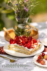 Rustic strawberry layer cake made from crepes, served al fresco. Summer sweetness and floral picnic mood.