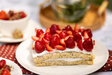 Strawberry crepe cake on a white plate, with wildflowers in the background. Sunny outdoor picnic.