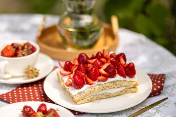 Golden crepes layered with whipped cream and strawberries. Summer dessert on a garden table.