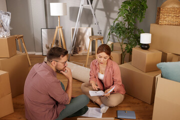 Two individuals sit on the floor of their new home, reviewing plans and discussing arrangements...