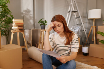A woman sits on the floor surrounded by moving boxes, feeling overwhelmed as she looks over...