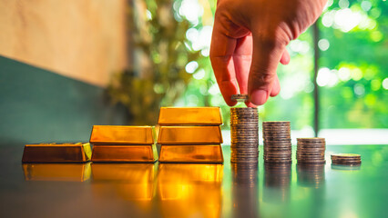 Investors are considering investing in gold by accumulating gold coins and stacking them higher and higher, with a pile of gold beside them. They view gold as the safest asset for investment.