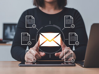 Businessman pressing holographic email button with floating document icons above laptop