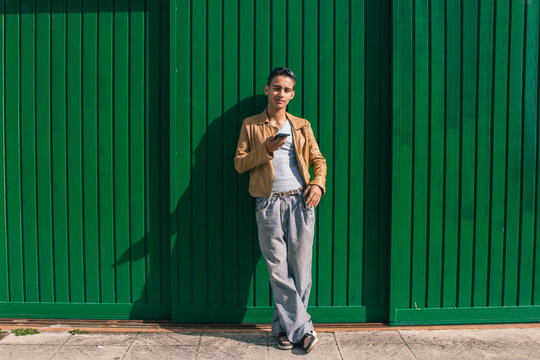 young urban man leaning against wall using mobile phone