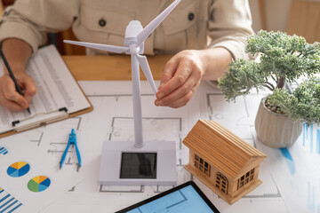 Engineer is working on sustainable housing project, incorporating wind turbine and solar panel technology for ecological future
