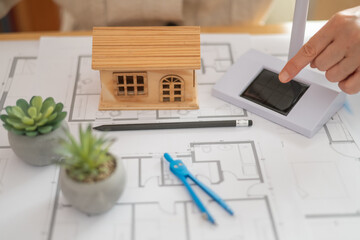 Architect pointing at a solar panel model while designing a sustainable house using blueprints and...