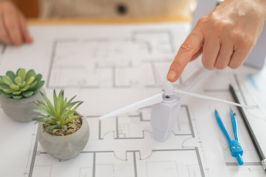 Engineer is placing a miniature wind turbine on blueprints, symbolizing the integration of renewable energy in residential architectural design