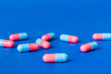 Heap of pink and blue pills on colored background. Tablets scattered on a table. Pile of red soft...