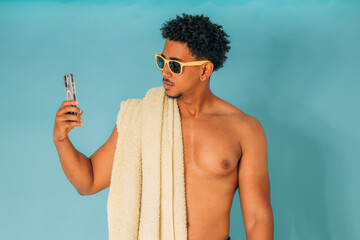 young latino man shouting, wearing sunglasses and a towel, isolated on white background, looking at his phone