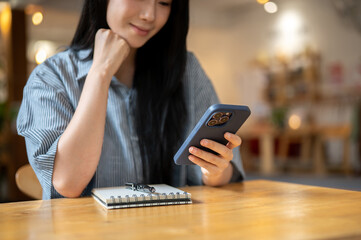 Asian woman resting head on hand watching video texting message on phone with notebook on cafe table