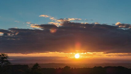 Breathtaking sunrise over a forested landscape with the sun peeking through dramatic clouds. Soft golden light spreading across the horizon, highlighting trees and hills in the early morning