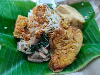 A portion of typical Indonesian pecel served on banana leaves, consisting of white rice, boiled vegetables (such as bean sprouts and cassava leaves), fried tempeh, fried tofu, omelette, and sprinkled 