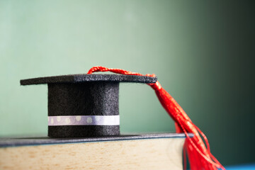 small mortarboard on top of hard cover book against chalkboard